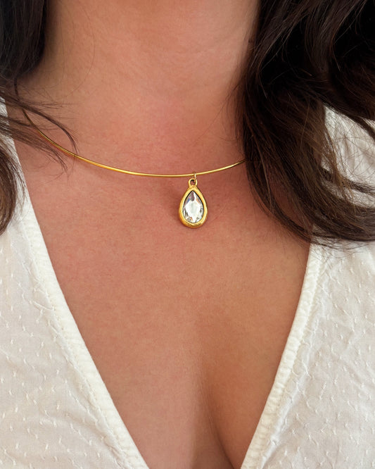 Gold wire necklace with a teardrop-shaped pendant on a person wearing a white top.