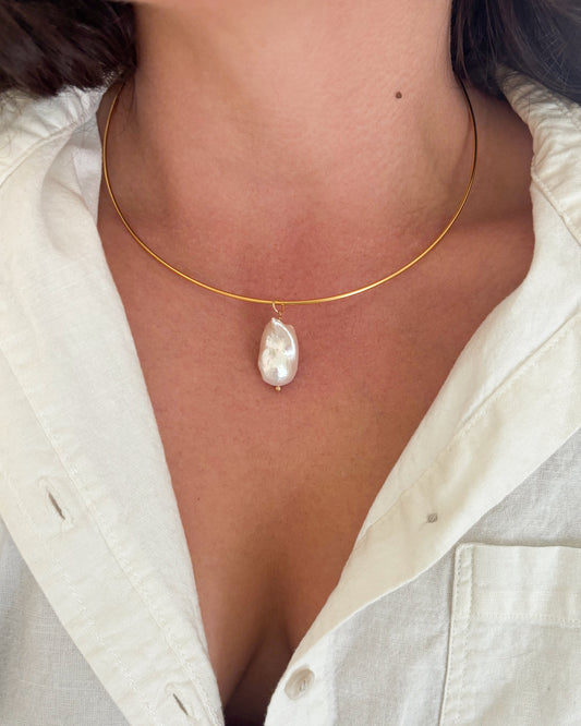 Gold wire necklace with a pearl pendant worn by a person in a white shirt.