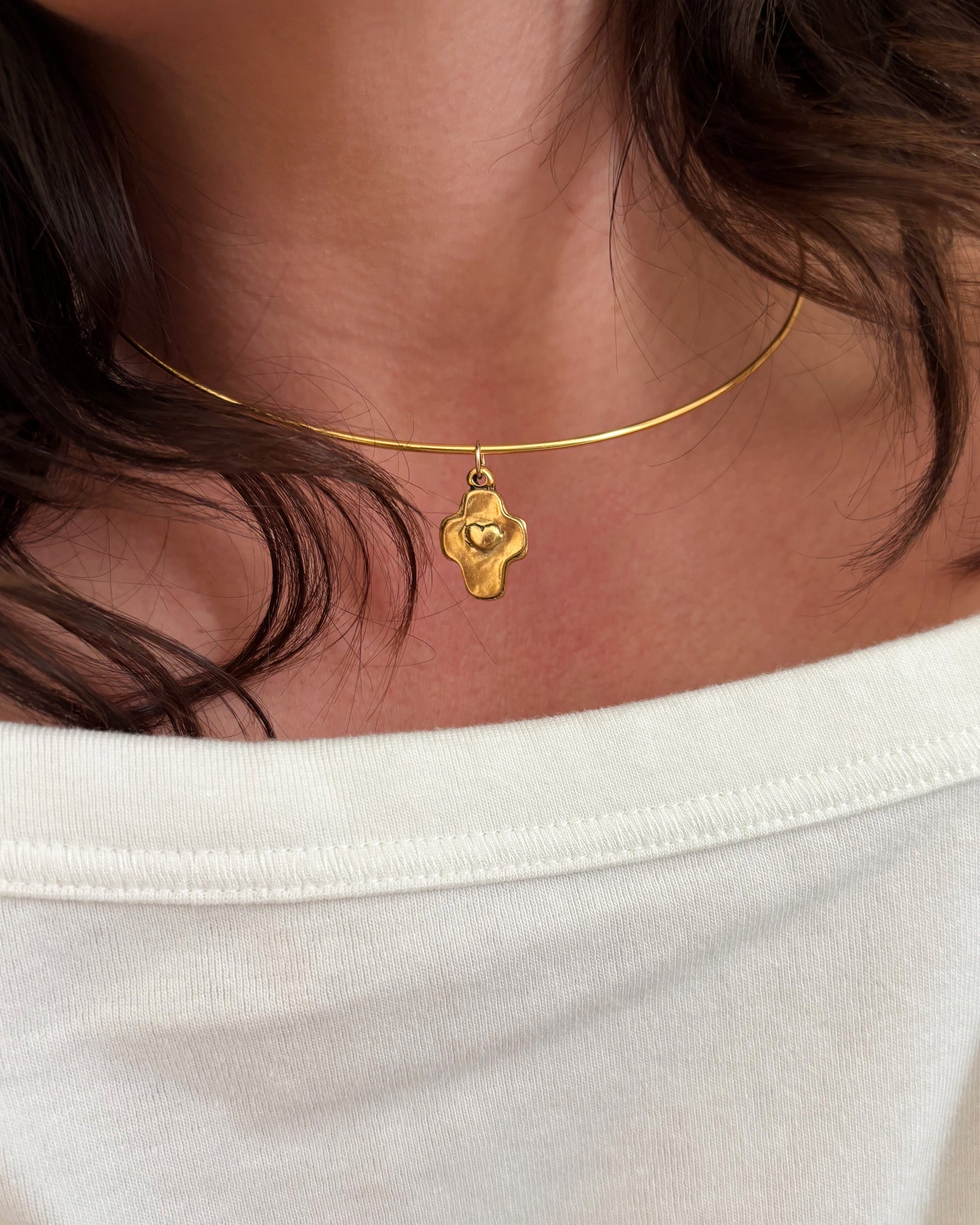 Gold wire necklace with a pendant worn by a person against a neutral background