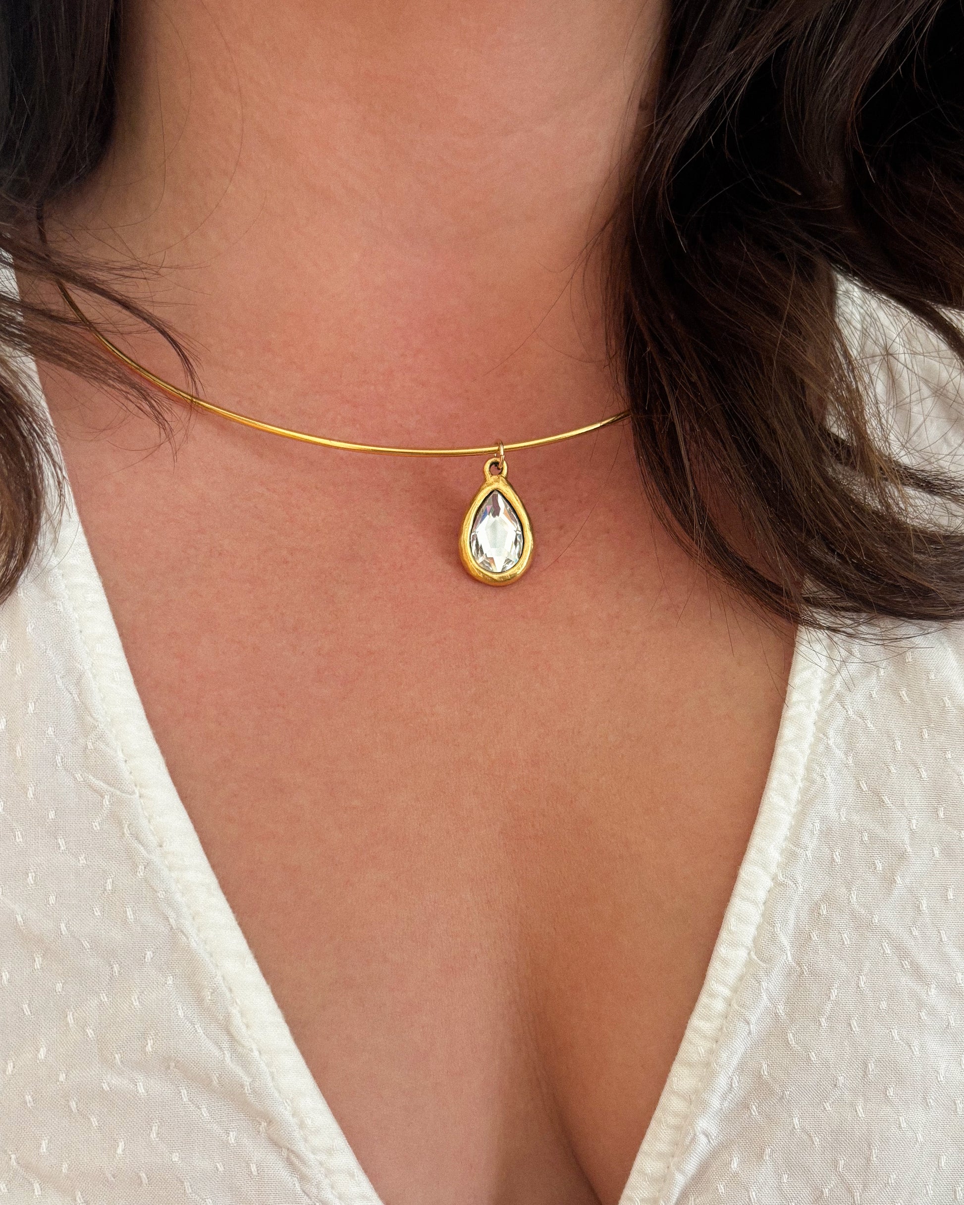 Gold wire necklace with a teardrop-shaped pendant on a person wearing a white top.